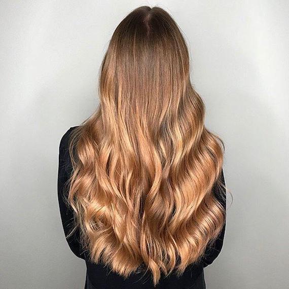 Model with long, wavy hair and warm blonde balayage, created using Wella Professionals.