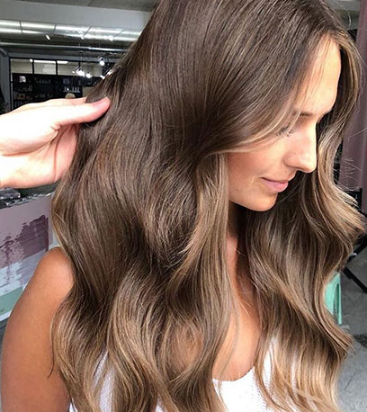 Side profile of woman with long, wavy hair in light chestnut brown, created using Wella Professionals