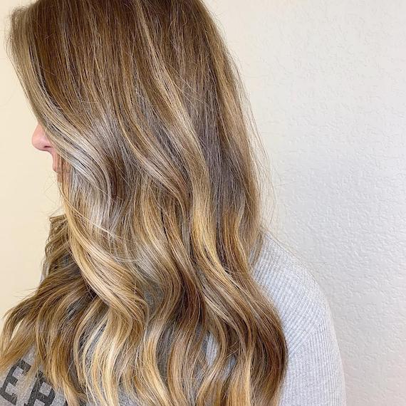 Seitenprofil eines Models mit langen, dunkelblonden Haaren und hellen Lowlights, kreiert von Wella Professionals.