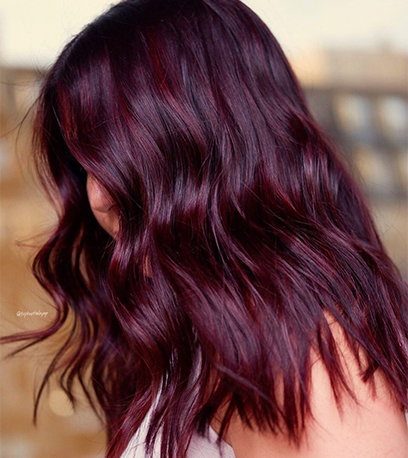 Side profile of woman with dark purple, wavy hair, created using Wella Professionals.