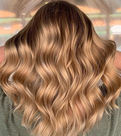 Hinterkopf einer Frau mit langem, goldblondem, gewelltem Haar, kreiert mit Wella Professionals.