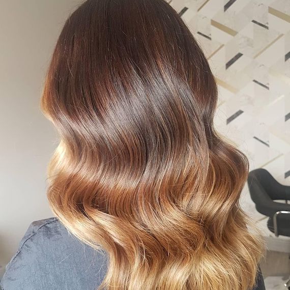 A person with long brown hair and a honey blonde ombre has their back facing the camera.