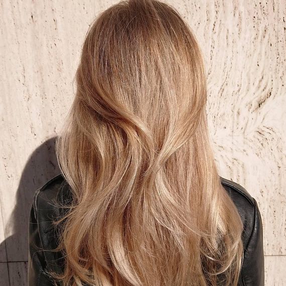 A person facing a speckled grey wall. They have long, golden honey blonde hair