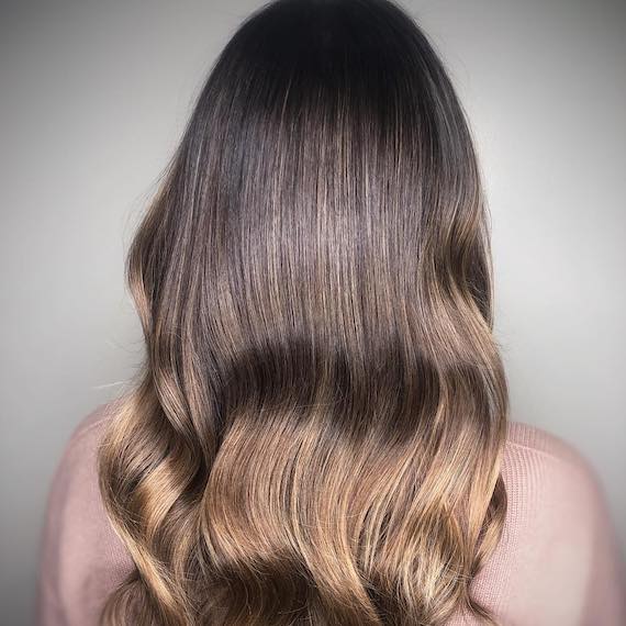 Frau mit gewelltem, dunklem honigblondem Haar, kreiert mit Wella Professionals.