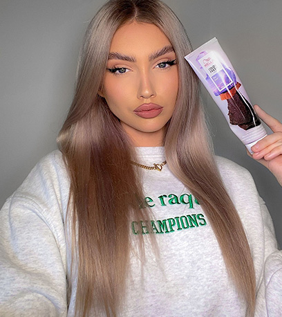 A person with long light lilac hair holds a bottle of Wella Professionals Colour Fresh Mask in shade Lilac Frost
