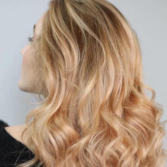 Hinterkopf einer Frau mit langem, gewelltem, kupfer-pfirsichfarbenem Haar, das mit Wella Professionals kreiert wurde.