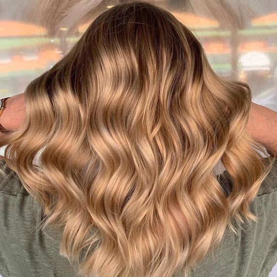 Hinterkopf einer Frau mit langem, gewelltem, verblasstem erdbeerblondem Haar, kreiert mit Wella Professionals.